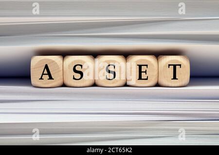Le mot Asset sur des cubes en bois contre pile de fichiers et dossiers arrière-plan. Concept de ressources commerciales, de comptabilité financière ou de gestion d'actifs. Banque D'Images