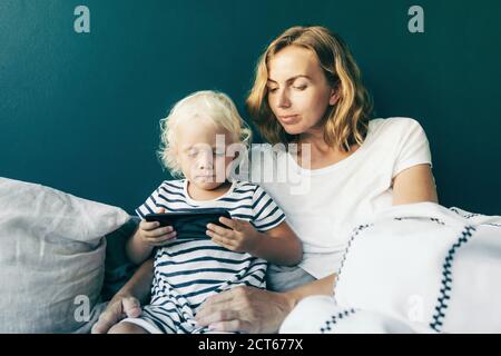 Jolie maman et petite fille dans un lit confortable avec mobile téléphone Banque D'Images