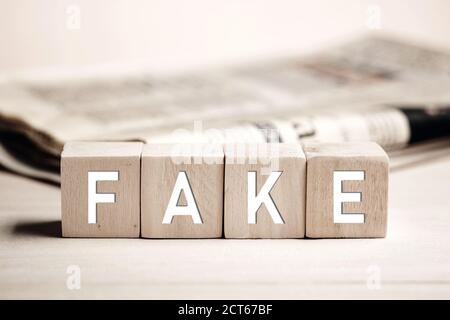 Le mot faux sur des blocs de bois avec un fond de journal. Fausses nouvelles dans les médias concept. Banque D'Images