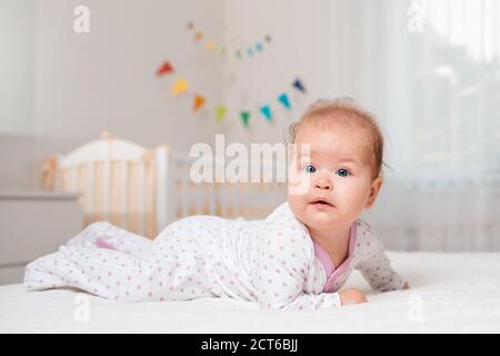 Un mignon bébé caucasien couché sur le lit. En arrière-plan, un berceau et des drapeaux colorés. Vue latérale. Le concept de s'occuper des enfants de la maternelle. Banque D'Images