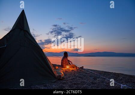 Un homme a installé sa tente et son camp et est assis sur les galets de la plage dedans avant de sa tente regardant le beau paysage Banque D'Images