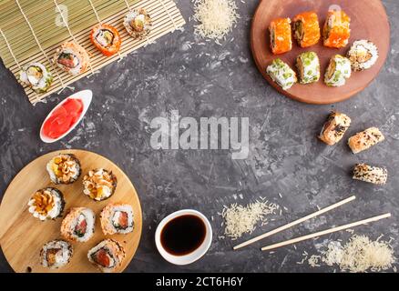 Différents types de sushis japonais maki avec saumon, sésame, fromage, roe et baguettes, sauce soja, gingembre mariné sur un backgrou en béton noir Banque D'Images