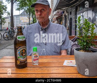 Un homme âgé qui a l'air attentif s'assoit à une table en plein air avec de la bière et un désinfectant pour les mains pendant la pandémie de Corona, Mitte, Berlin Banque D'Images