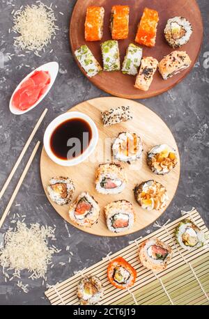 Différents types de petits pains à sushis maki avec saumon, sésame, fromage, roe et baguettes, sauce soja, gingembre mariné sur fond de béton noir. Haut v Banque D'Images