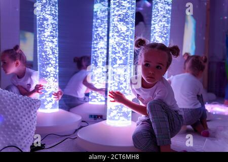 Enfant en salle de thérapie stimulante sensorielle, snoezelen. Enfant autiste en interaction avec des lumières colorées lampe à tube à bulle pendant la séance de thérapie. Banque D'Images