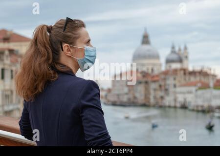 Voyage pendant la pandémie de Covid-19. Élégante femme d'âge moyen avec masque médical explorant les attractions sur le pont de l'Accademia à Venise, Italie. Banque D'Images