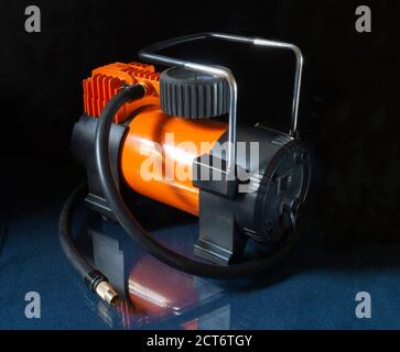 Compresseur de voiture sur table en verre avec réflexion, équipement avec corps orange sur fond noir Banque D'Images