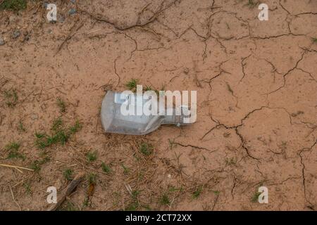 Petite bouteille de liqueur en plastique écrasée posée sur la boue sèche mise au rebut du sol et pollution de l'environnement Banque D'Images