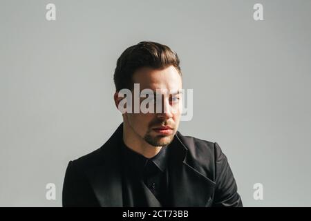Jeune homme beau en costume noir, regardant sérieusement la caméra, sur fond de studio Uni Banque D'Images