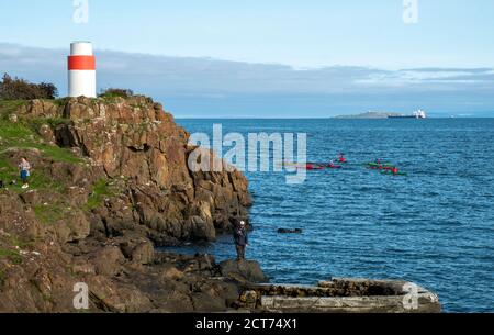 Les kayakistes de mer passent tandis que les gens pêchent à partir d'un affleurement rocheux sur la côte de Fife près d'Aberdour, en Écosse. Banque D'Images