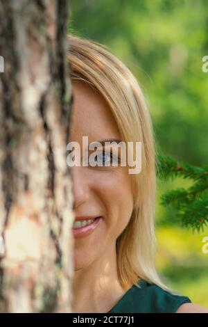 Blue Eyes femme blonde souriant et se cachant derrière le tronc de pin. Style de couleur vintage. Les yeux sont en mode de mise au point de la caméra Banque D'Images