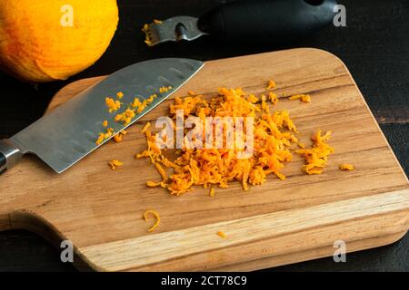 Zesting an Orange: Zeste d'orange sur une planche à découper en bois Banque D'Images