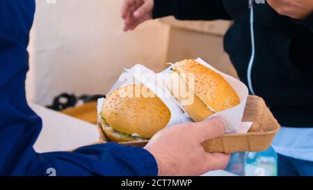 Gros plan de l'homme en tenant les mains des hamburgers à Street Food Festival. La cuisine en plein air, gastronomie, la nourriture à emporter, les gens et notre concept de service Banque D'Images