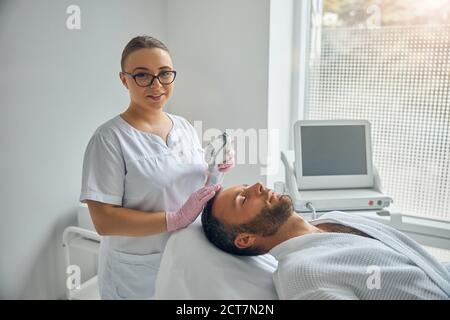 Beau jeune homme recevant un traitement laser facial dans l'armoire de cosmétologie Banque D'Images