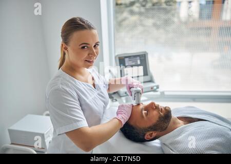 Un cosmétologue souriant traitant la peau masculine avec un appareil laser Banque D'Images