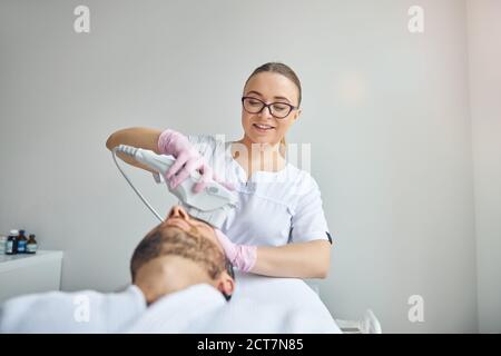 Cosmétologue gai traitant la peau masculine avec un dispositif laser Banque D'Images