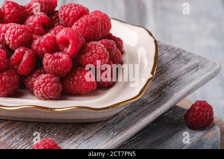 Fruits à la framboise dans une assiette sur de vieilles planches à découper, pile saine de baies d'été sur fond de bois gris, vue en angle macro Banque D'Images