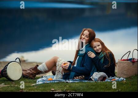 Une jeune femme et une fille aux cheveux longs rouges, assise sur une couverture en automne. Banque D'Images