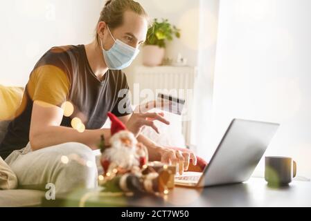 Homme avec masque protecteur à la maison shopping en ligne avec carte de crédit pour Noël. Banque D'Images