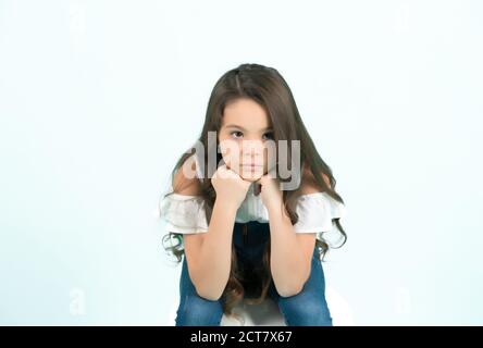 Kid prop menton sur les mains sur fond bleu. Fille avec de longs cheveux de brunette en jeans dans l'ensemble. La beauté, la mode, l'apparence, le concept, l'espace de copie Banque D'Images