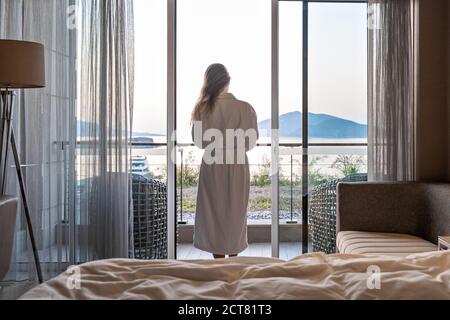 Belle femme de derrière en peignoir debout sur la terrasse de Chambre d'hôtel avec vue sur la mer lever du matin Banque D'Images