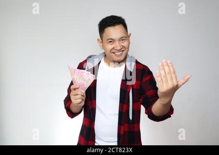 Portrait d'un jeune indonésien heureux tenant de l'argent rupiah, sourire riant le geste gagnant, sur fond blanc Banque D'Images