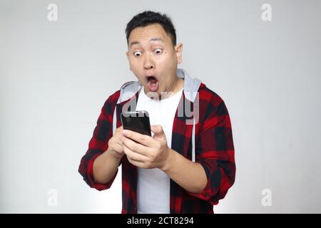 Beau jeune homme asiatique lisant des SMS bavardant sur son téléphone, choqué expression surprise Banque D'Images