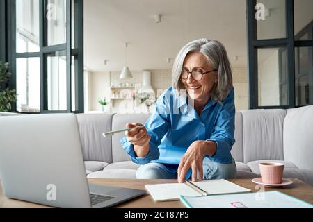 Une femme mûre et heureuse appelle sur un ordinateur portable, travaillant à domicile. Banque D'Images