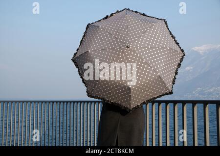 Femme penchée sur une rampe sur le front de mer avec un parasol. Banque D'Images