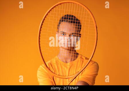 Photo en studio d'un jeune joueur de tennis tenant une raquette contre arrière-plan orange Banque D'Images