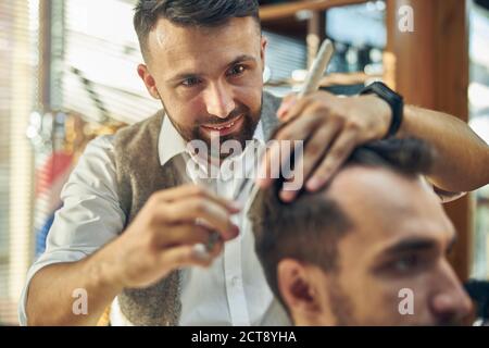 Tondeuse à cheveux gaie donnant à son client une coupe de cheveux Banque D'Images