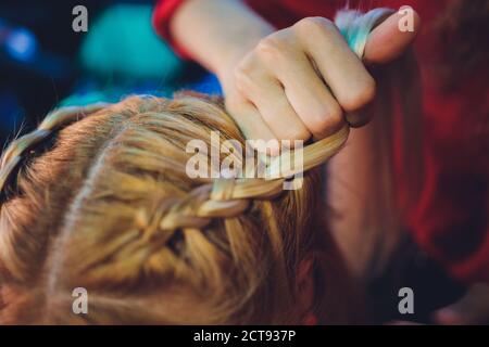 Processus de tressage le maître tisse des tresses sur sa tête blonde petite fille dans le salon de beauté gros plan. Soins professionnels des cheveux et création de coiffures. Banque D'Images