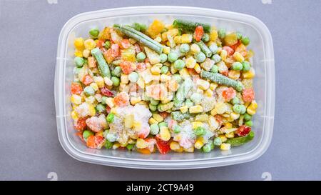 Légumes mélangés congelés dans un récipient en plastique pour un stockage à long terme. Congélation profonde des légumes. Légumes surgelés sur fond gris. Banque D'Images