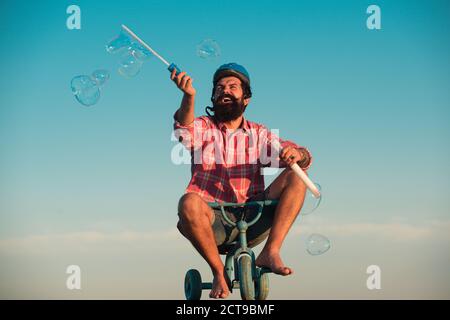 Mémoire d'enfance. Portrait d'un homme barbu comme un hipster fou s'amusant avec le vélo dehors. Banque D'Images