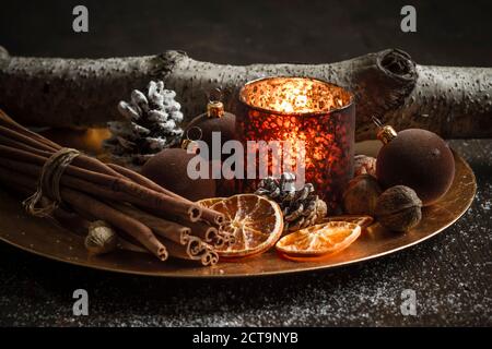 Décoration de Noël avec bougie chauffe-plat, boules d'arbre de noël, bâtons de cannelle, tranches d'oranges séchées et noix sur l'assiette, prise studio Banque D'Images