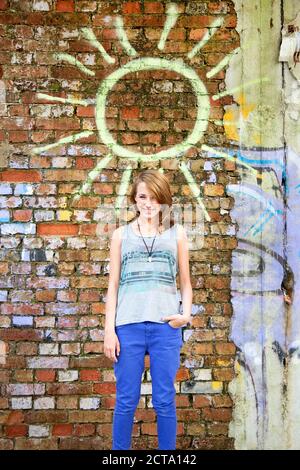 Allemagne, Berlin, Portrait of teenage Girl standing in front of wall avec graffiti, smiling Banque D'Images