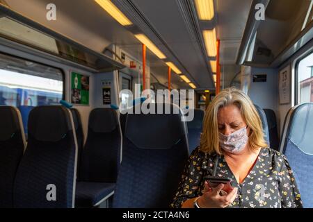 Une femme d'âge moyen assise seule dans une voiture de train porter un masque facial pendant la pandémie du coronavirus Banque D'Images