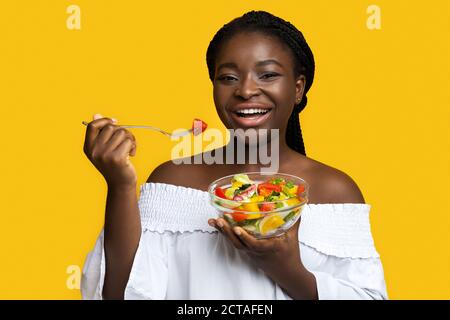 Une nutrition saine. Bonne femme noire mangeant de la salade de légumes frais sur fond jaune Banque D'Images