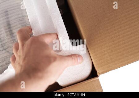 Emballage des marchandises dans une boîte en carton avec du matériau en mousse de polystyrène pour le transport sécuritaire des marchandises. Isolé sur fond blanc. Les mains de l'homme sont l'emballage de la goo Banque D'Images