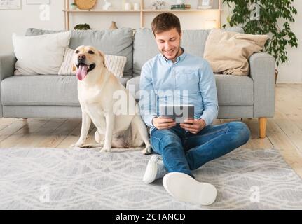 Jeune homme à la maison avec une tablette et un chien Banque D'Images