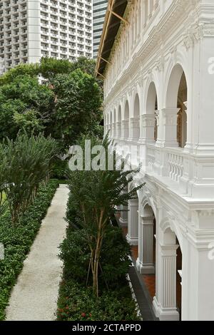 Une vue en perspective d'une rangée d'arches dans un ancien bâtiment colonial blanc contrastait avec un bâtiment moderne de plusieurs étages. Banque D'Images