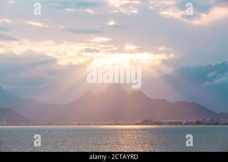 Vue panoramique de la plage de Konyaalti turc célèbre sur le coucher du soleil. Les rayons de soleil percent les nuages et illumine les montagnes. Antalya, Turquie Banque D'Images