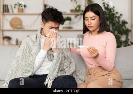 Petite amie qui traite un Boyfriend malade qui donne un médicament assis sur un canapé à l'intérieur Banque D'Images