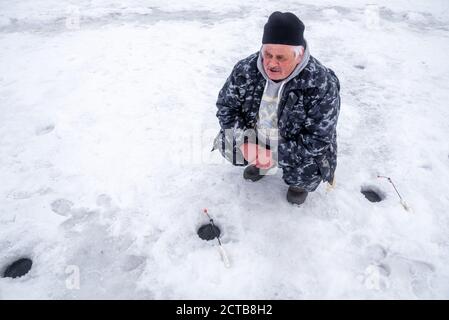 Un pêcheur est assis et se concentre sur la pêche dans un trou sur la glace de la rivière. Banque D'Images