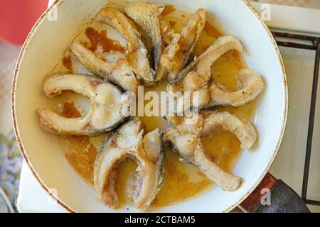 Les morceaux de poisson sont frits dans une casserole blanche. Morceaux de carpe frits. Cuisiner à la maison. Banque D'Images