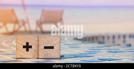 Signes plus et moins sur des cubes en bois sur un paysage de plage paisible. Business en ligne, achat en ligne alternatives concept d'évaluation Banque D'Images