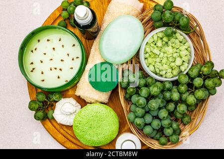 Accessoires de spa naturels et raisins verts placés sur une assiette en bois. Des ingrédients frais pour des soins personnels sains et confortables. Fond en béton de pierre, Banque D'Images