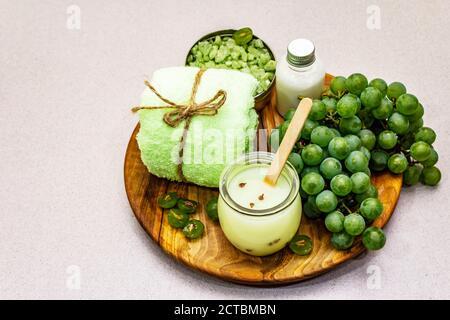 Accessoires de spa naturels et raisins verts placés sur une assiette en bois. Des ingrédients frais pour des soins personnels sains et confortables. Fond en béton de pierre, Banque D'Images