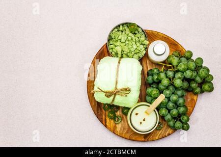 Accessoires de spa naturels et raisins verts placés sur une assiette en bois. Des ingrédients frais pour des soins personnels sains et confortables. Fond en béton de pierre, Banque D'Images