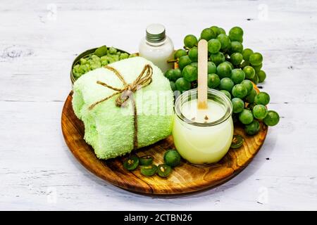 Accessoires de spa naturels et raisins verts placés sur une assiette en bois. Des ingrédients frais pour des soins personnels sains et confortables. Panneau arrière en bois blanc Banque D'Images